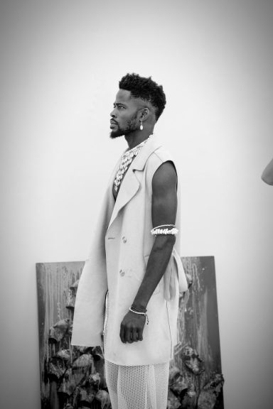 Hombre de perfil en atuendo blanco, con peinado moderno y fondo artístico difuminado.